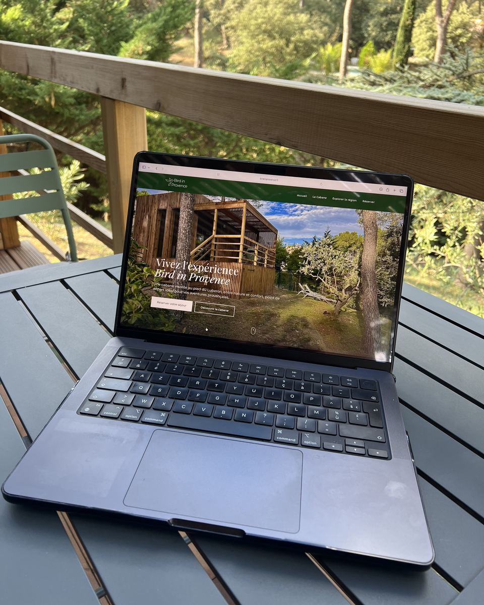 Le site de Bird in Provence, réalisé par L'Étoile du Web, sur un ordinateur portable posé sur une table de terrasse en bois, sous les pins